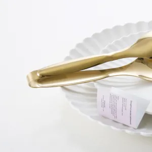 Nordic style gold stainless steel steak and BBQ food tongs presented on a white plate