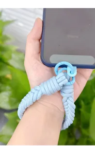 Close-up of a light blue braided phone wrist strap with a round metal clip shown on a hand