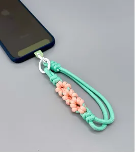 Detailed view of a braided daisy phone wrist strap in mint green and peach pink.