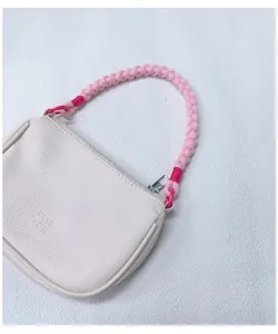Close-up view of a pink hand-woven rope handle on a minimalist cream leather handbag