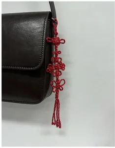 Detail eines traditionellen roten chinesischen Knotens mit Quaste an einer braunen Ledertasche