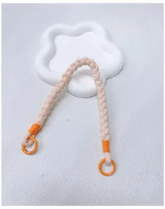 Detailed macro view of a handmade braided beige and orange phone wrist strap with metal rings