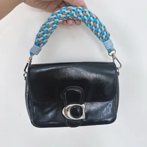 Detalle de un bolso de cuero negro con un asa trenzada a mano de colores vivos