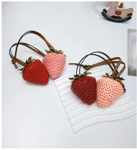 Detailed macro view of high-simulation red and pink strawberry bag charms with leather straps