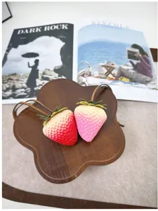 Detailed macro view of two 3D realistic strawberry bag charms on a wooden board