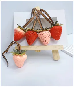 Close-up of realistic strawberry bag charms with brown leather straps on a wooden easel