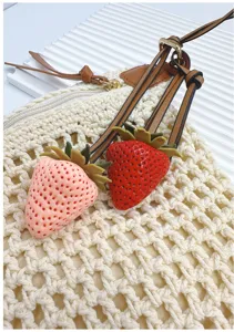 Realistic red and pink strawberry pendants hanging on a white handmade woven bag