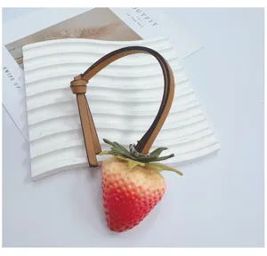 Realistic strawberry bag charm with brown leather strap and detailed fruit texture