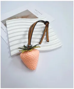 Realistic pink strawberry bag charm with elegant tan leather strap accessory detail