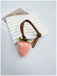Detailed macro view of realistic pink strawberry bag charm with brown leather strap.