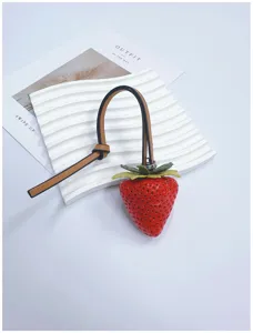 Realistic strawberry bag charm with textured details and tan leather strap