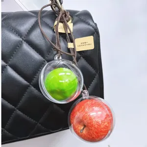 Detail view of realistic red and green apple bag charms hanging on a black quilted bag