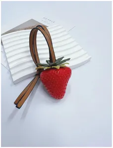 Close-up of a realistic 3D simulation strawberry bag charm with brown leather strap