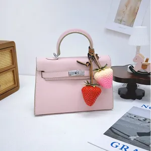 Elegant pink Kelly style handbag featuring realistic red and pink strawberry bag charms