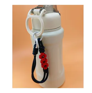 Detail view of a hand-woven red daisy flower paracord wrist strap lanyard on a bottle