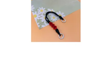Hand-braided black phone wrist strap with red floral decor and white metal rings.