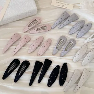 Gros plan de pinces à cheveux à pois rose, gris et noir sur un tissu blanc soyeux.