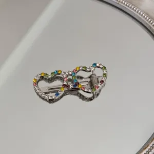 Detail of rhinestone heart-shaped hair clip with colorful crystals on a mirror.