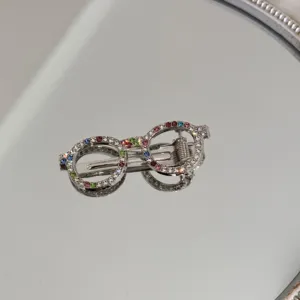 Macro view of a silver-toned glasses-shaped hair clip adorned with colorful rhinestones