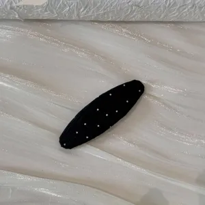Vue rapprochée d'une jolie pince à cheveux ovale à pois noirs avec texture en tissu doux