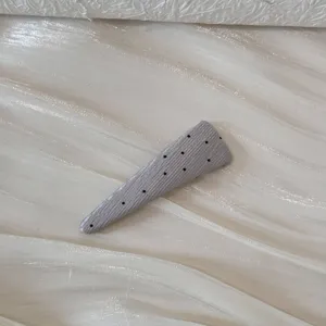 Gros plan d'une pince à cheveux grise à pois sur un tissu blanc texturé élégant