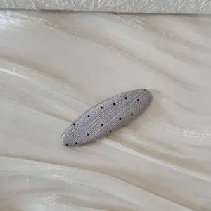 Gros plan d'une pince à cheveux ovale gris argenté avec pois noirs et texture