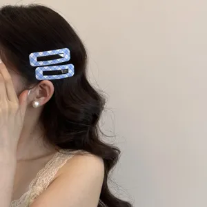 Dettaglio di fermagli per capelli rettangolari a scacchi blu e bianchi su capelli scuri