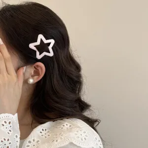 Détail d'une pince à cheveux BB rose en forme d'étoile ajourée sur cheveux ondulés