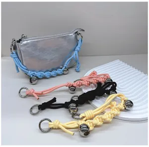 Hand-woven bag straps in assorted colors with decorative metal bells on a display.