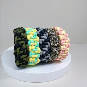 Hand-woven multi-color paracord survival bracelets displayed on a minimalist white stand