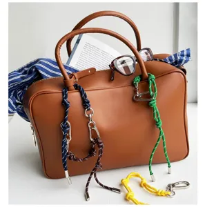 Detailed close-up showing colorful woven rope bag charms with carabiners on a brown bag