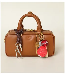 Detailed view of a brown leather handbag featuring stylish braided charms and a carabiner hook