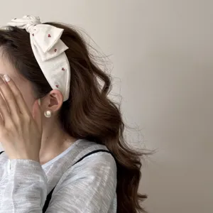 Detail view of a white fabric headband with cherry patterns and a cute bow design.
