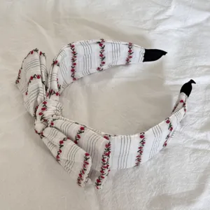 Macro detail of a white fabric headband featuring cute red cherry patterns and a large bow