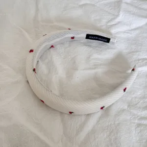 Close-up detail of a sweet white plaid fabric headband featuring red cherry embroidery