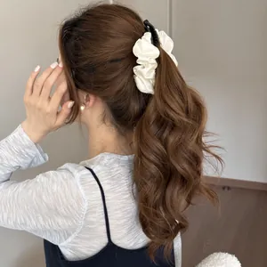 Close-up of a white pleated satin banana clip used on a wavy brown ponytail.