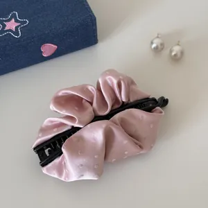 Detailed view of a pink satin banana clip with white polka dots and pleated fabric texture.