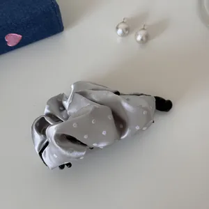 Close-up of elegant silver satin pleated banana clip with white polka dots for women