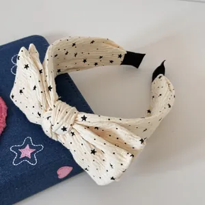 Gros plan sur un serre-tête en tissu crème avec motifs étoiles noires et joli nœud