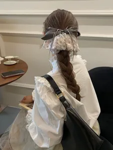 Détail d'une élégante pince à cheveux nœud gris et dentelle rose sur une tresse.