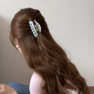Vista trasera de una pinza para el pelo a cuadros azules sujetando un semirecogido en pelo castaño