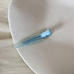 Vue détaillée d'une pince à cheveux triangulaire bleu clair mat avec texte gravé