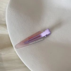 Détail macro d'une pince à cheveux bec de canard dégradé violet et rose sur une assiette
