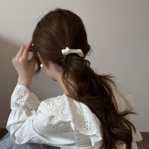 Detail shot of a cream-colored double-layer fabric bow hair tie on a low ponytail.