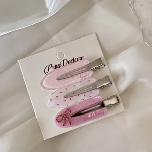 Detail of three pink acrylic duckbill hair clips with floral and bow patterns