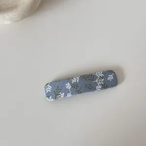 Détail d'une pince à cheveux rectangulaire recouverte d'un tissu floral bleu et olive