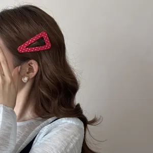 Détail d'une pince à cheveux triangulaire rouge à pois sur des cheveux bruns ondulés