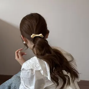 Detail view of a minimalist cream fabric bow hair tie worn on a ponytail hairstyle.