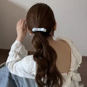 Back view of a woman wearing a light blue fabric double-layer bow hair tie on wavy hair