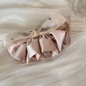 Close-up view of a champagne satin and organza ruffled hair clip with crystal accents